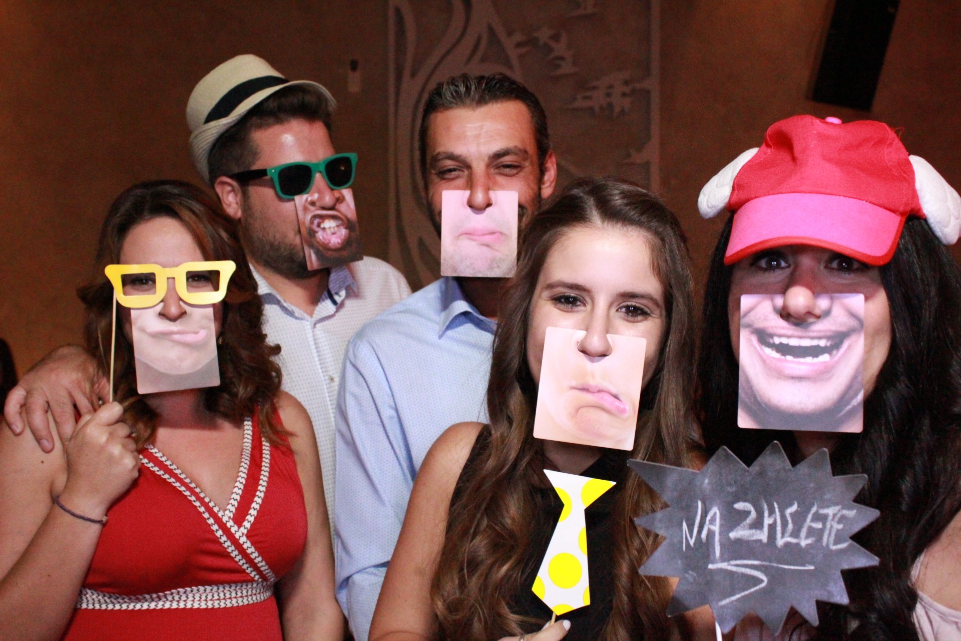 Group of five people wearing humorous face masks and props, including colorful glasses, hats, and a sign that says 'NA ZHGETE'.